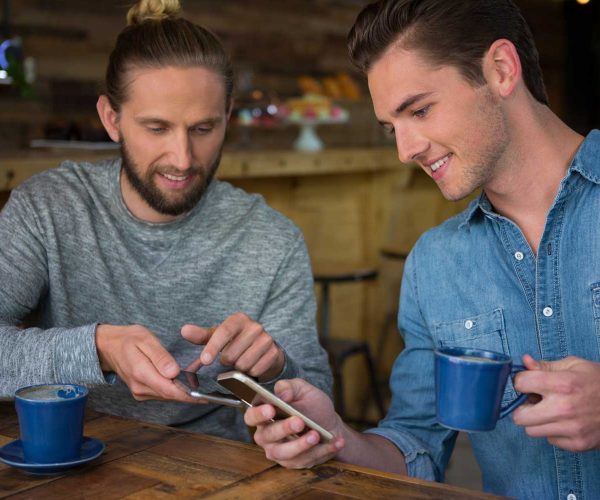 happy-male-friends-using-smart-phone-in-coffee-hou-X58RU7Q.jpg
